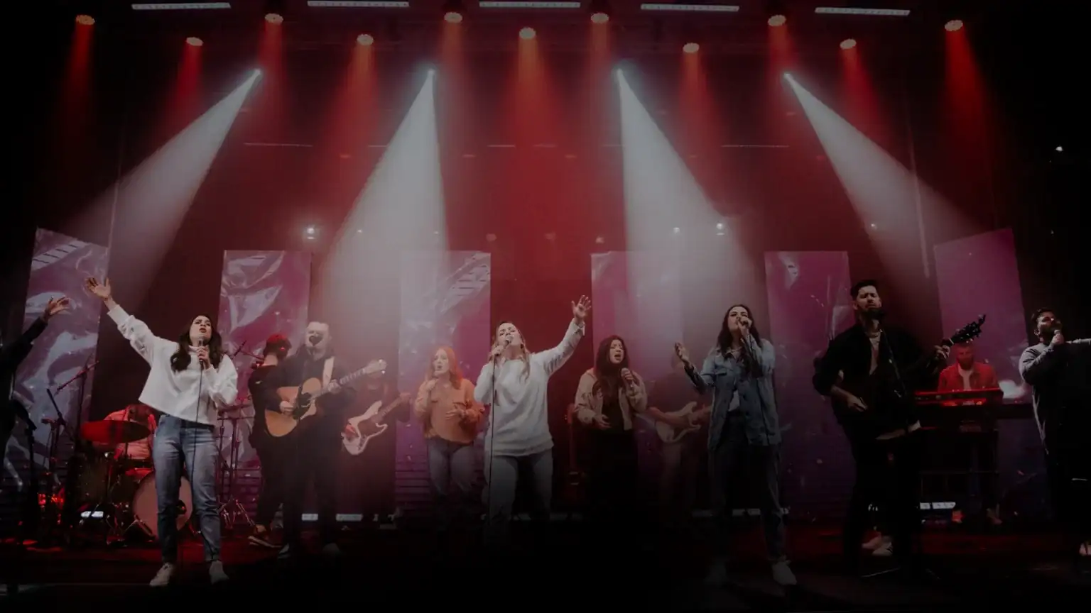 Equipe de louvor cantando no palco, com banda completa e luzes de show
